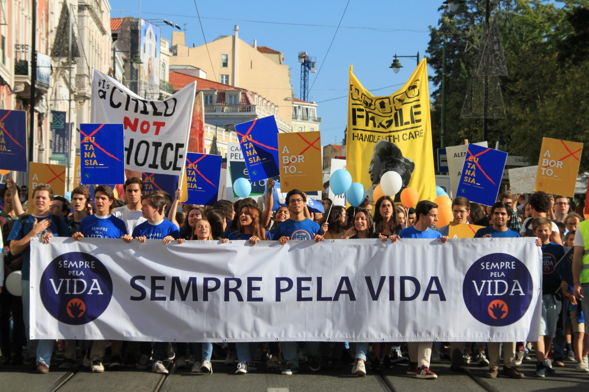 Multidão da Marcha pela Vida a descer uma rua de Lisboa, com famílias, jovens e cartazes.